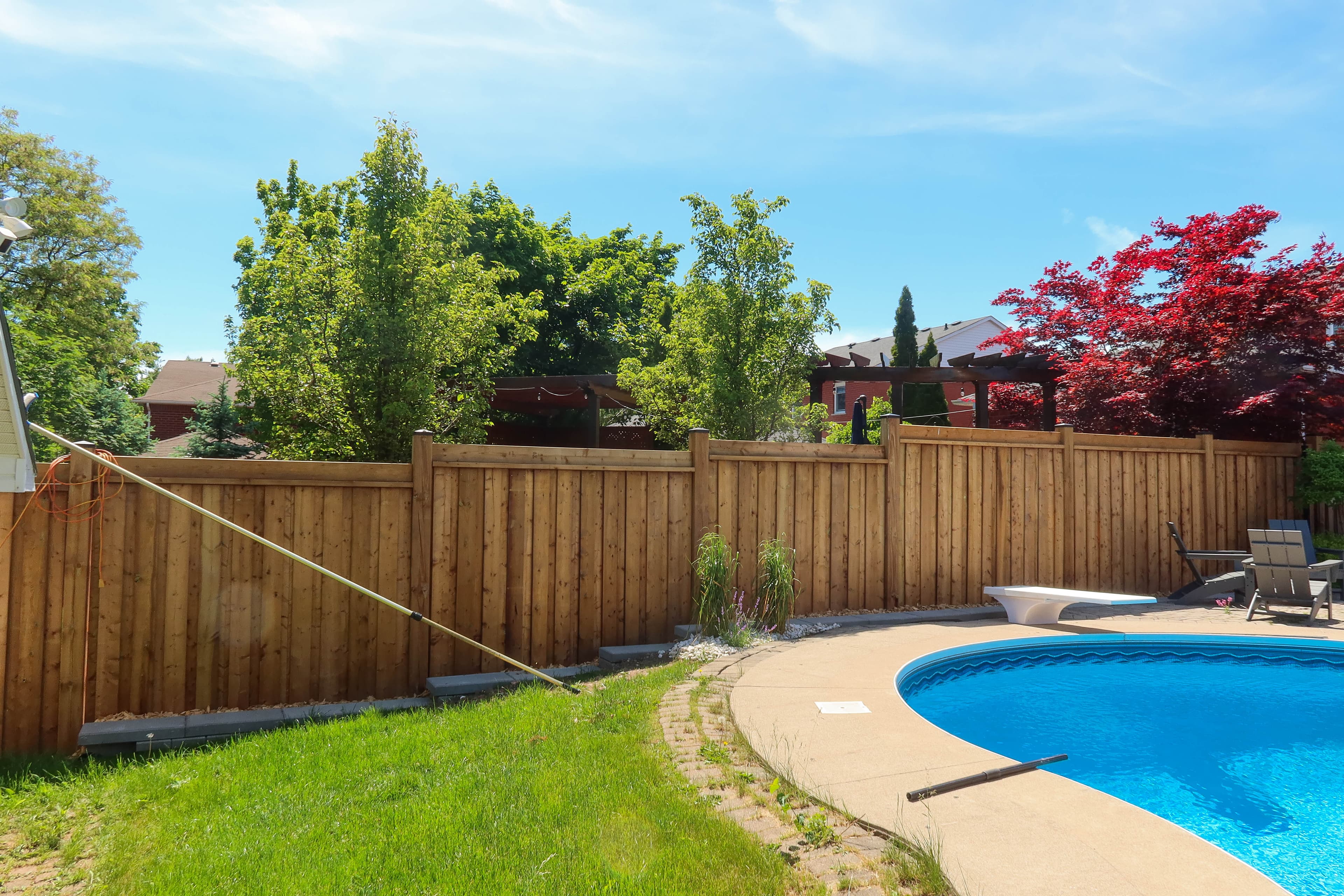 Long pressure treated wood privacy fence curving around an inground pool with a landscaped bed in Burlington
